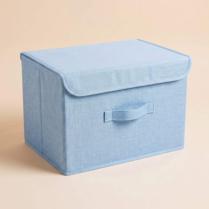 Fabric Storage Bin with Lid – Foldable in Light Blue – closed lid flap overhanging the front, soft shadow on peach surface