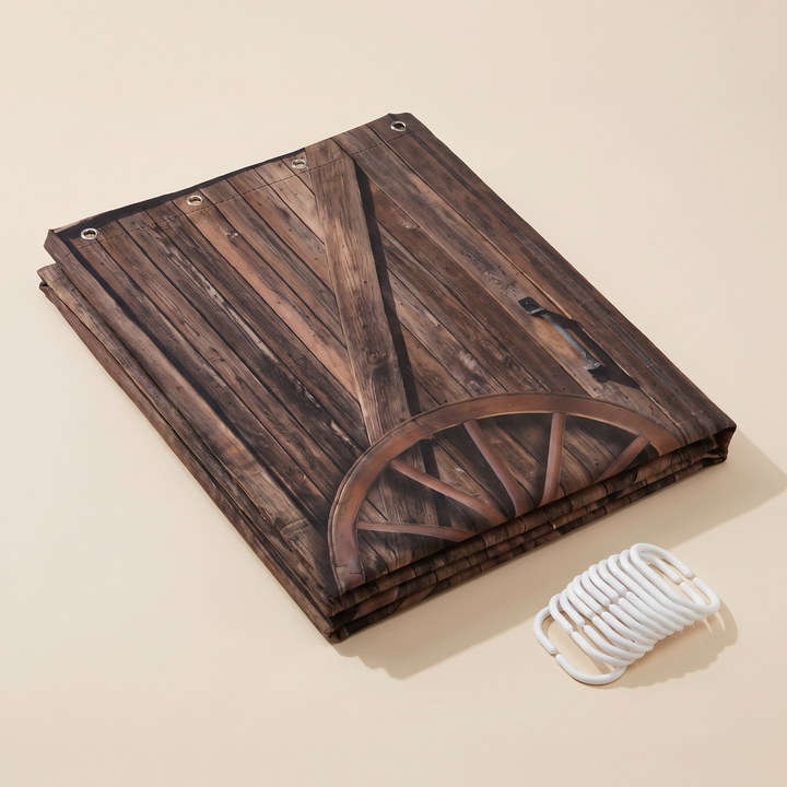 Farmhouse Shower Curtain – Rustic Barn Door Print in Brown – Barn Doors &amp; Wagon Wheel – folded flat on a beige surface with white plastic hooks beside it