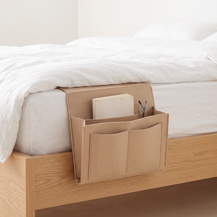 Felt Bedside Caddy – 5 Pockets in Beige – hanging over the side of a wooden bed holding a book and glasses