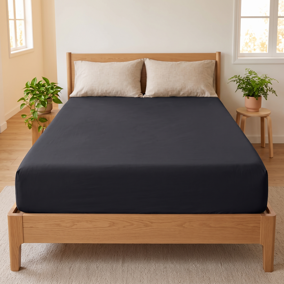 Fitted Sheet in Black – straight-on front view flanked by potted plants, two pillows above