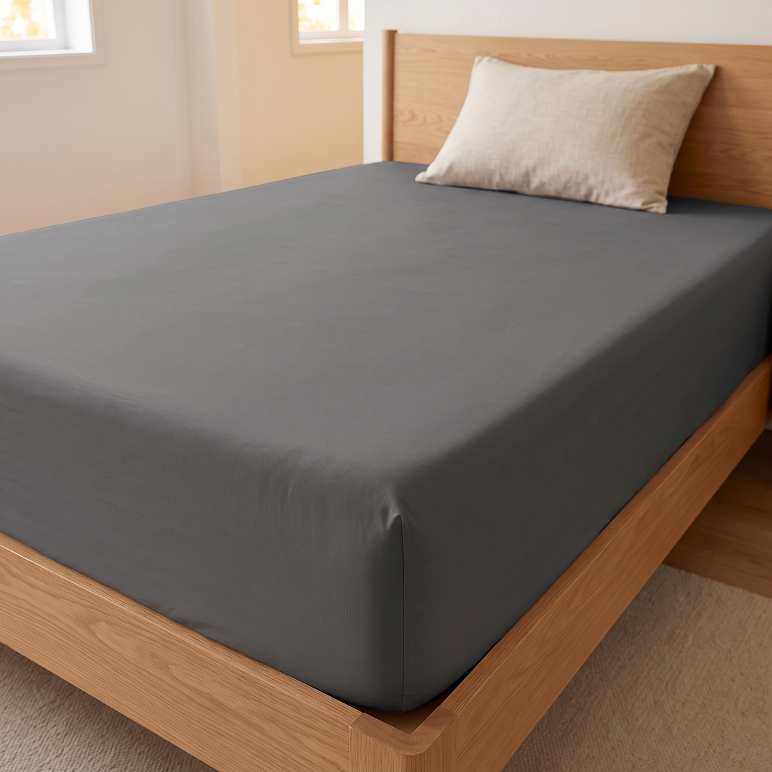 Fitted Sheet in Dark Gray – angled view with one beige pillow at wooden headboard