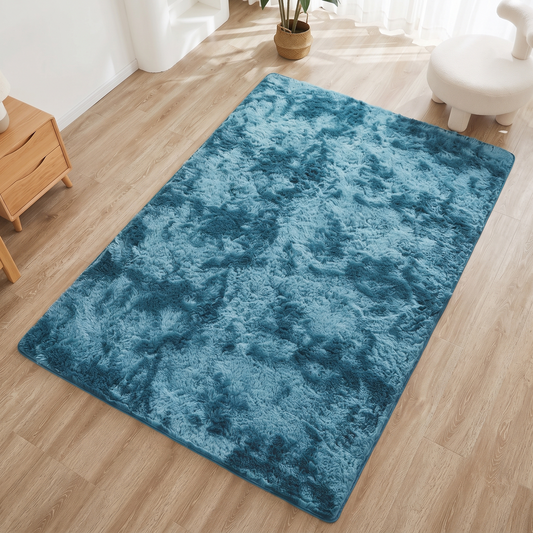Fluffy Shag Rug in Aqua – Tie-Dye – on sunlit wood floor beside a white rounded stool