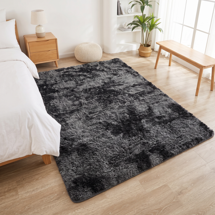Fluffy Shag Rug in Dark Gray – Tie-Dye – between a bed and wooden bench, woven pouf behind