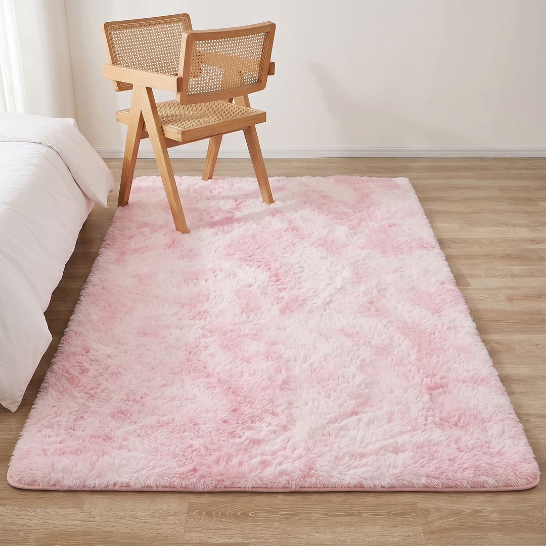 Fluffy Shag Rug in Pink – Tie-Dye – under a rattan wood chair on a wood floor beside a bed