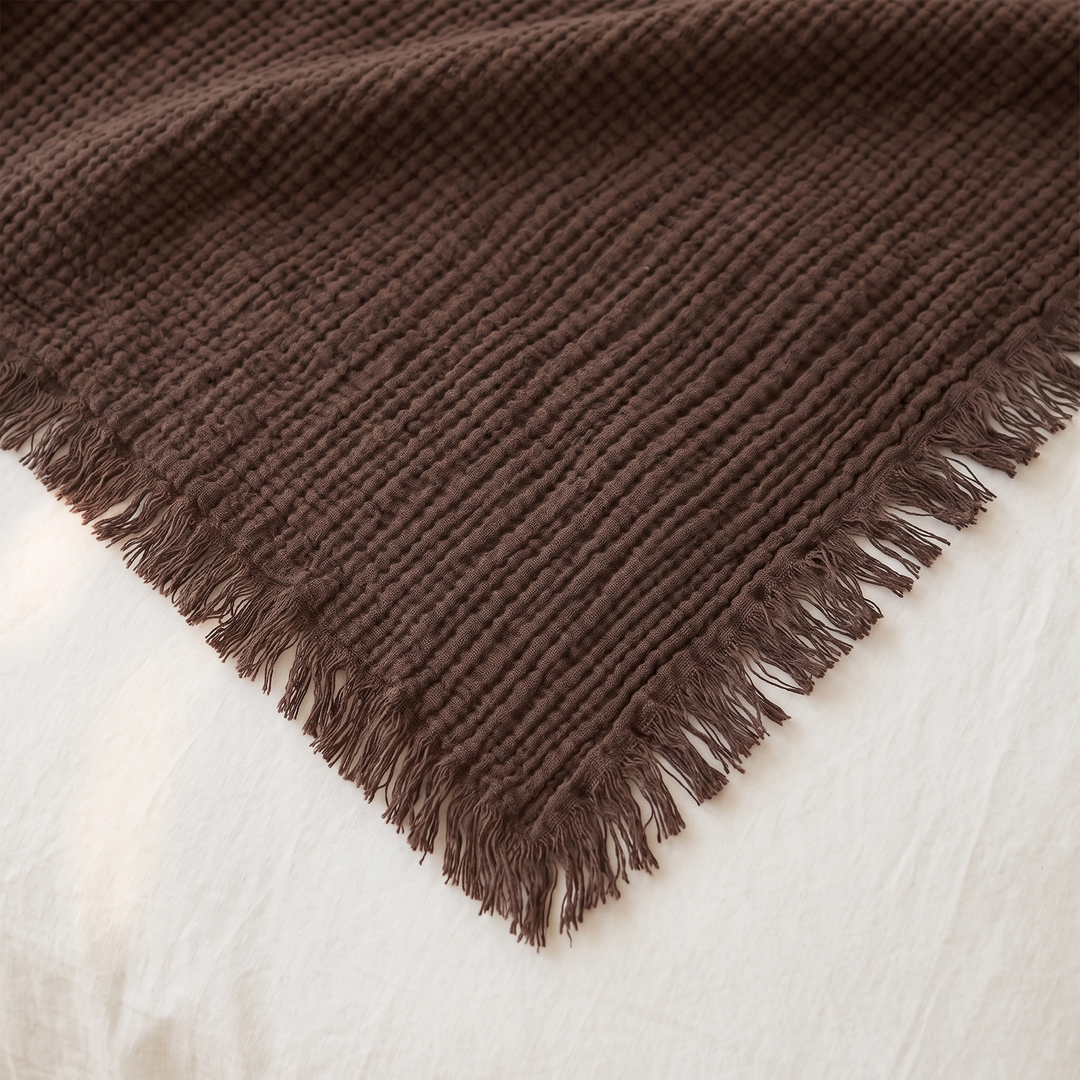 Crinkled Cotton Blanket with Fringe in Dark Brown – close-up of one fringed corner and textured weave on white bedding