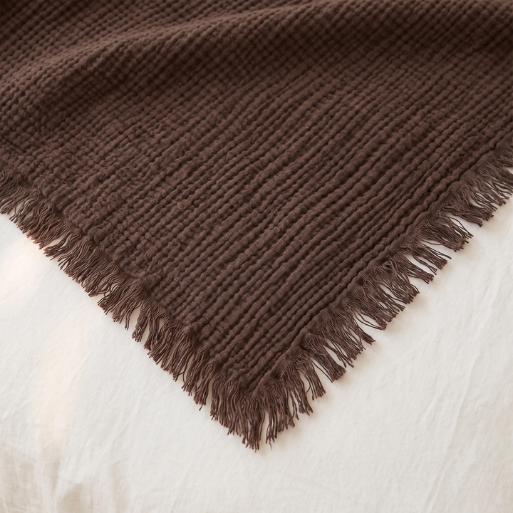 Crinkled Cotton Blanket with Fringe in Dark Brown – close-up of one fringed corner and textured weave on white bedding