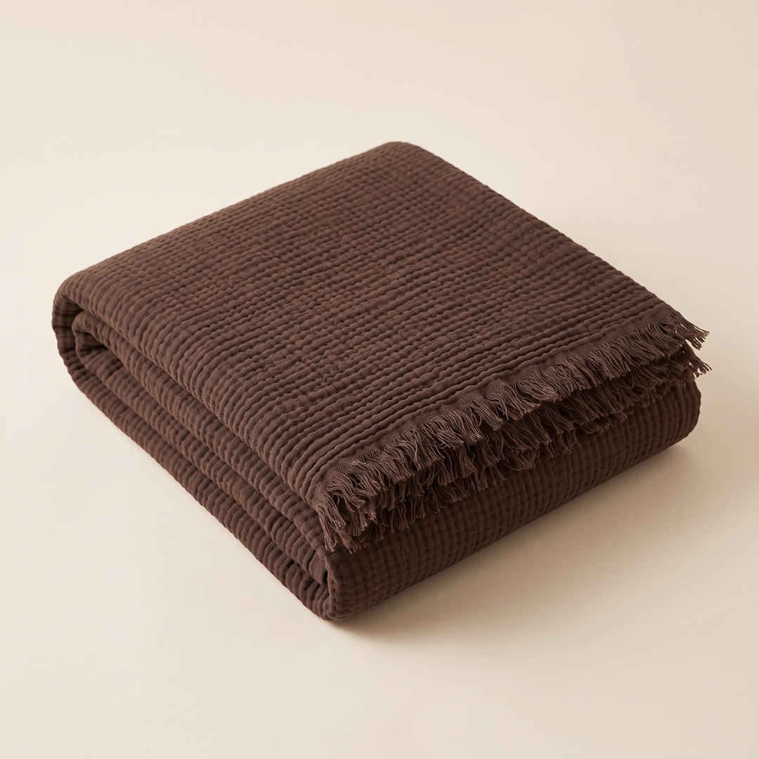 Crinkled Cotton Blanket with Fringe in Dark Brown – folded neatly in a stack on a plain cream background