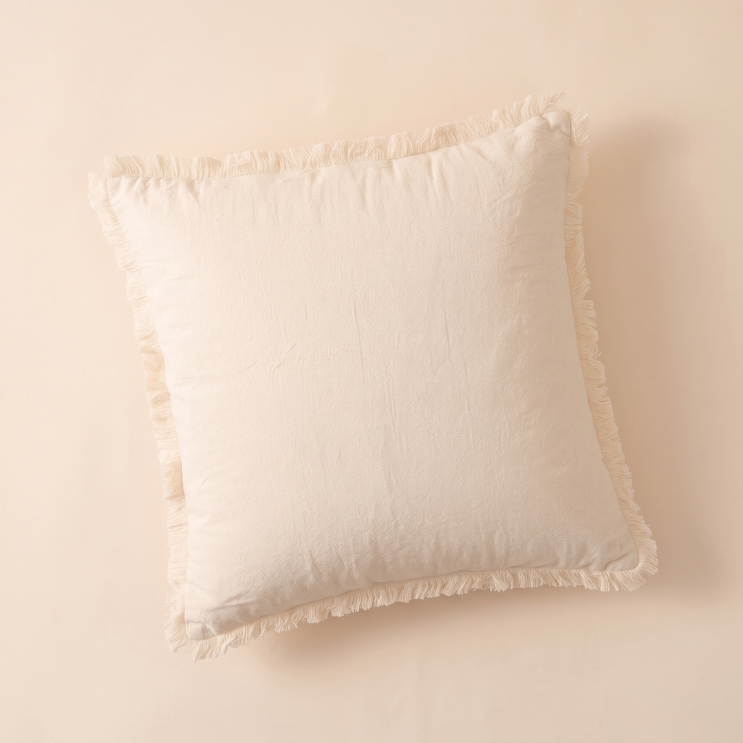 Fringed Pillow Cover in Cream – flat lay from above on a plain peach surface