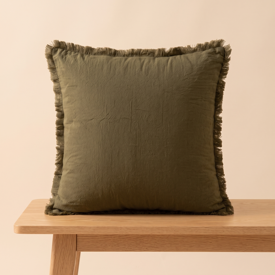 Fringed Pillow Cover in Dark Olive – resting on a light wood bench with legs visible below