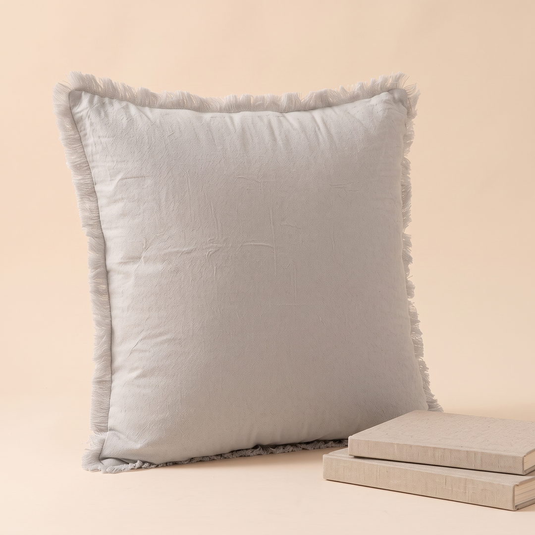 Fringed Pillow Cover in Light Gray – angled view propped beside two stacked books