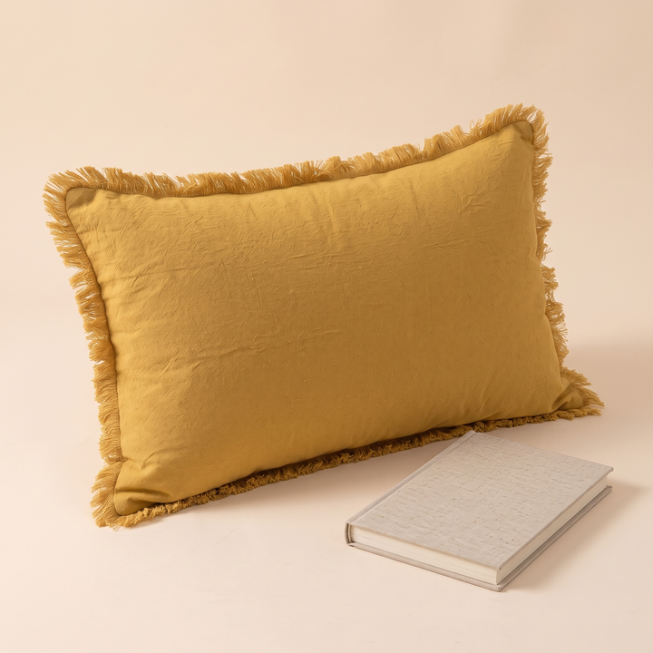 Fringed Pillow Cover in Mustard – upright with a single closed hardcover book resting in front