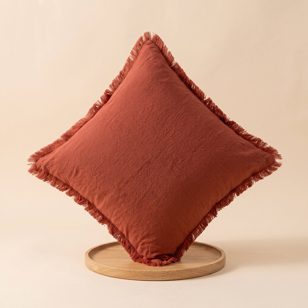 Fringed Pillow Cover in Rust – balanced on one corner on a round wooden tray