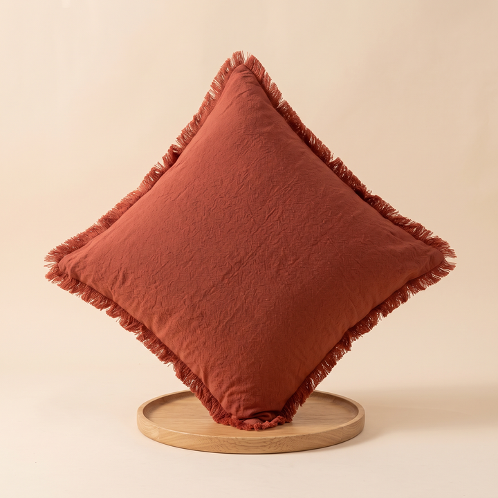 Fringed Pillow Cover in Rust – balanced on one corner on a round wooden tray