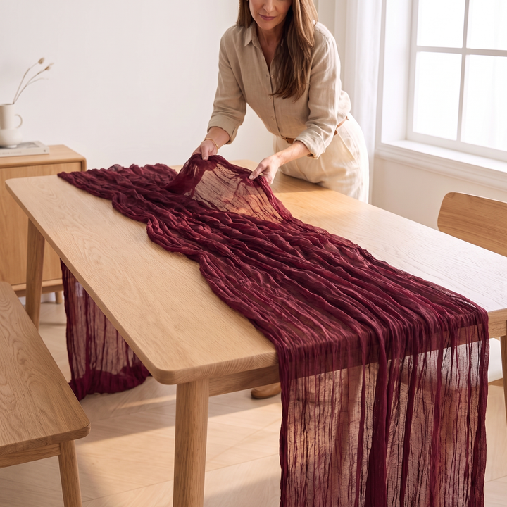 Gauze Table Runners – Set of 4 in Burgundy – being smoothed down the center of an oak dining table