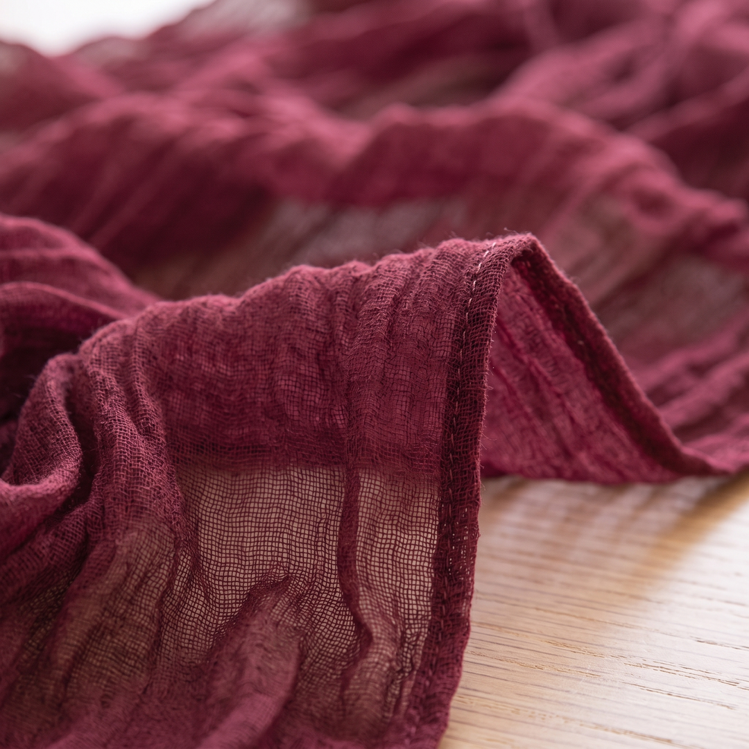 Gauze Table Runners – Set of 4 in Burgundy – close-up of the hemmed edge and loose, crinkled weave on a wooden surface