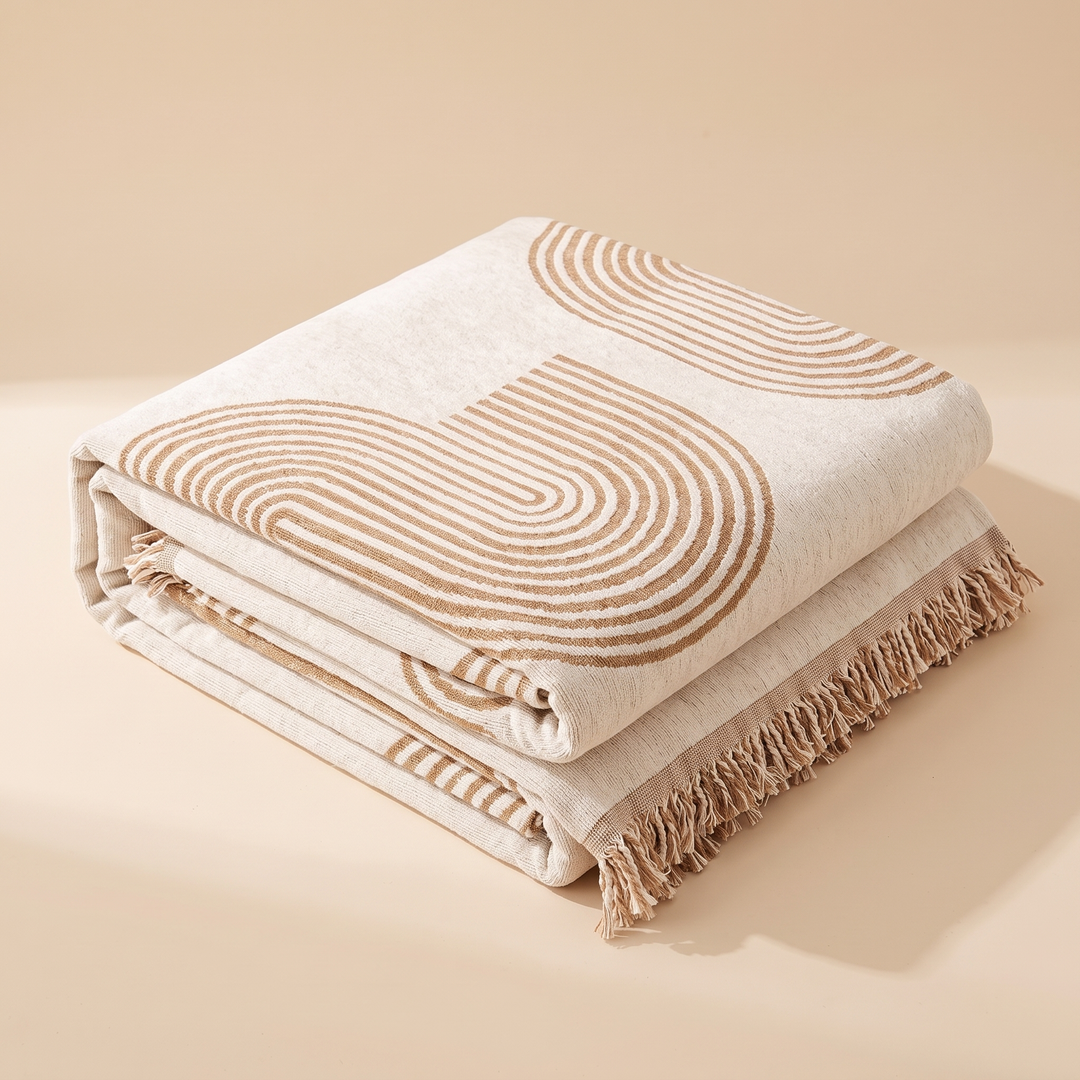 Geometric Chenille Couch Cover with Fringe in Beige – Arch – folded neatly in a stack on a plain peach backdrop