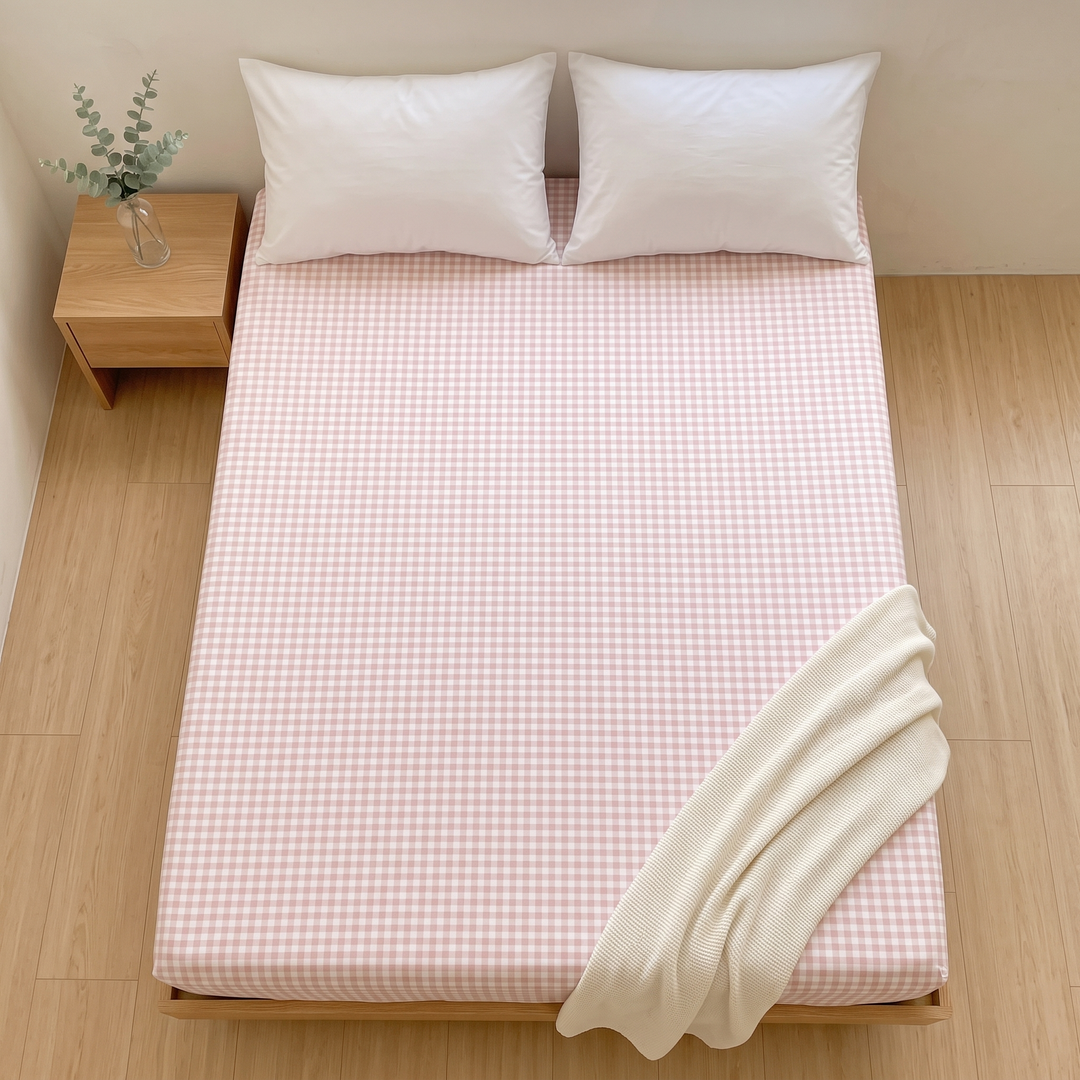 Gingham Fitted Sheet in Pink Gingham – top-down view with cream knit blanket across one corner