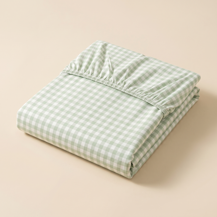 Gingham Fitted Sheet in Green Gingham – neatly folded with elastic edge visible on a plain beige background