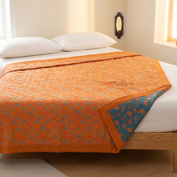 Ginkgo Leaf Gauze Blanket in Orange – spread over a made bed with corner folded back