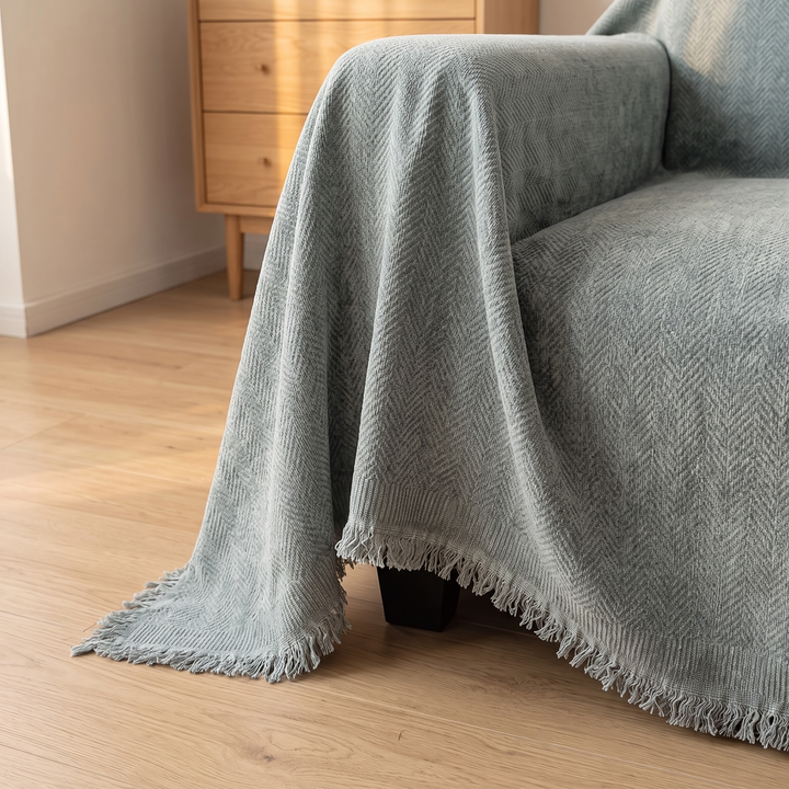 Herringbone Chenille Couch Cover with Fringe in Gray – hanging over an armchair arm, fringed hem beside a wooden dresser