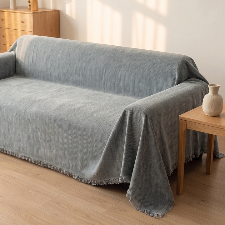 Herringbone Chenille Couch Cover with Fringe in Dusty Blue – side view beside a wooden side table with a ceramic vase