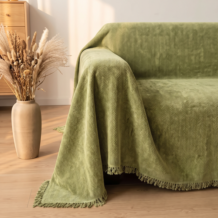 Herringbone Chenille Couch Cover with Fringe in Olive Green – corner view beside a tall vase of dried pampas grasses