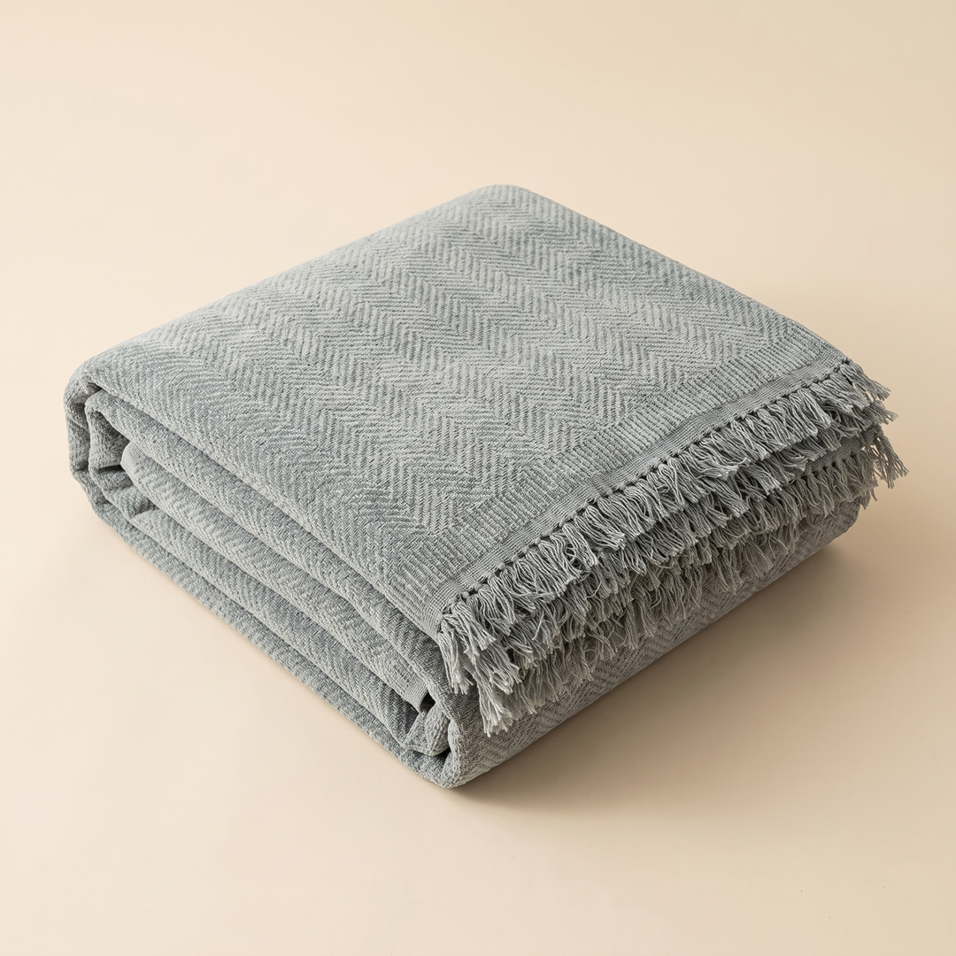 Herringbone Chenille Couch Cover with Fringe in Gray – folded neatly in a stack on a plain beige background