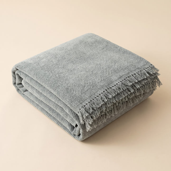 Herringbone Chenille Couch Cover with Fringe in Gray – folded neatly in a stack on a plain beige background