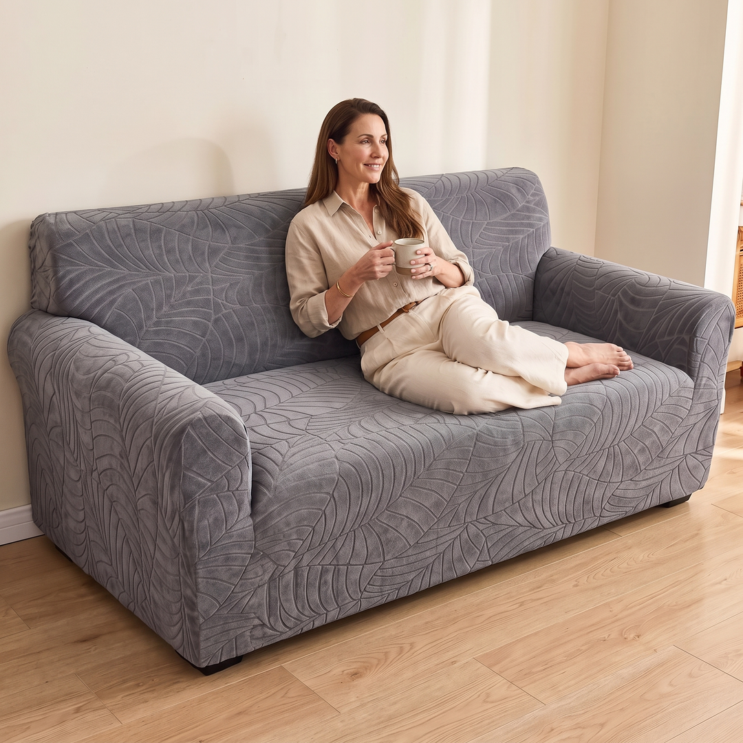 Jacquard Stretch Sofa Cover in Dark Gray – woman relaxing with a mug on a covered sofa in a sunlit living room