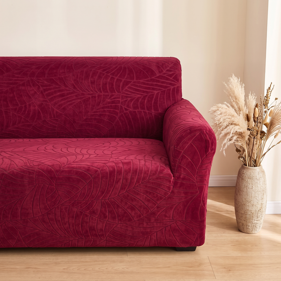 Jacquard Stretch Sofa Cover in Burgundy – beside a textured vase of dried pampas grass in sunlight