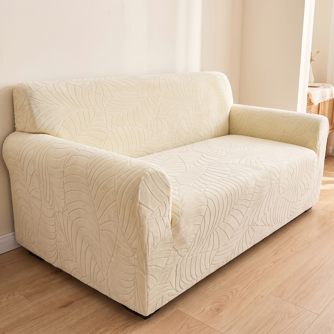 Jacquard Stretch Sofa Cover in Cream – angled view on wood flooring beside a wicker table