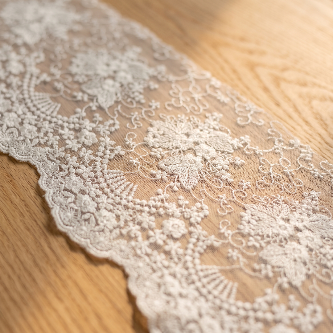 Lace Table Runner in White – close-up of embroidered floral lace edge on a wooden surface