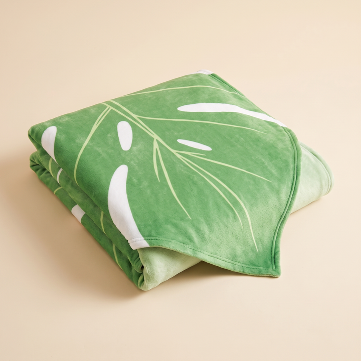 Leaf Blanket – Leaf-Shaped Flannel Throw in Green – Monstera – folded in a neat stack on a plain beige background