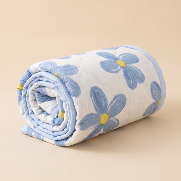 Lightweight Floral Quilt in Blue Floral – rolled up into a tight cylinder on a plain beige background