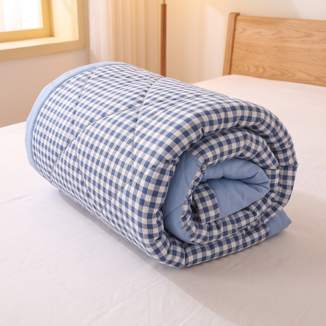 Lightweight Quilted Coverlet in Blue Gingham – rolled into a tight cylinder on a white-sheeted bed