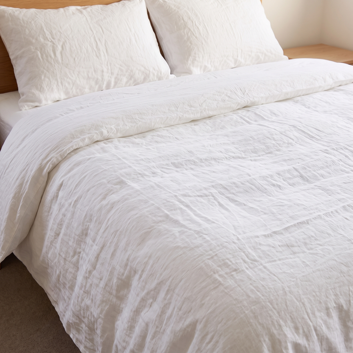 Linen Duvet Cover Set in White – on a made bed with two pillows beside a wooden nightstand
