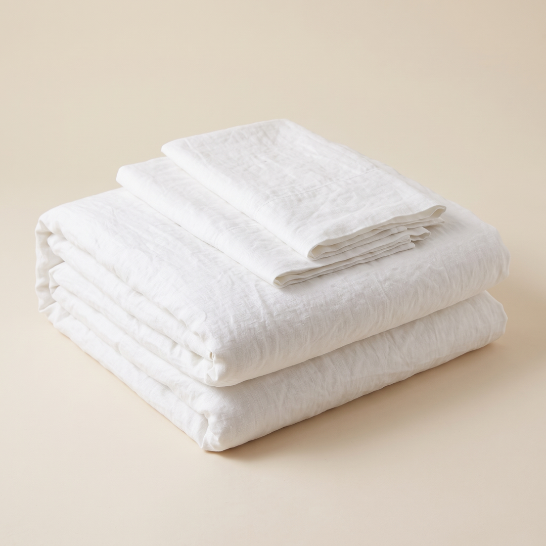 Linen Duvet Cover Set in White – folded stack with two pillowcases on top, plain beige backdrop