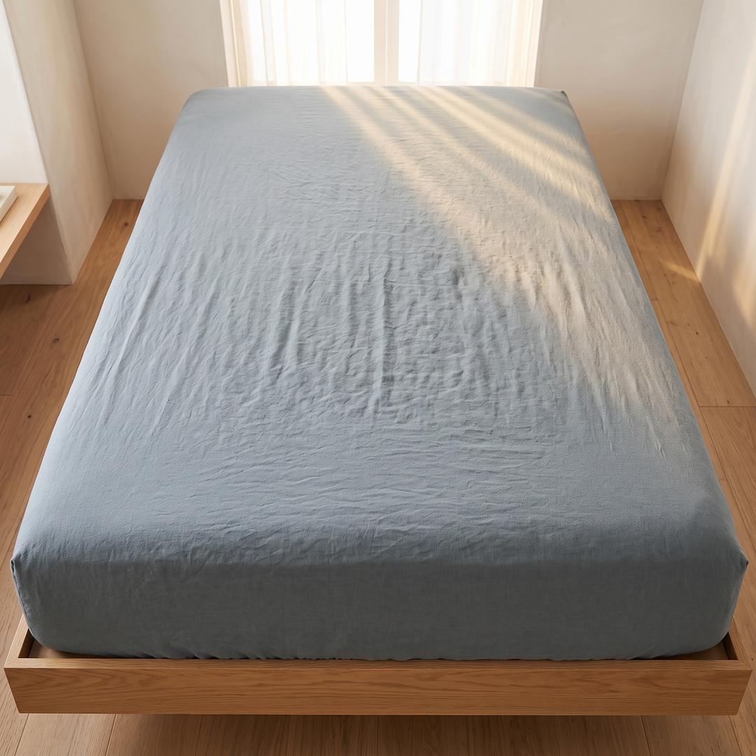 Linen Fitted Sheet – Deep Pocket in Dusty Blue – overhead view of fitted bed with sunlight streaks through sheer curtains