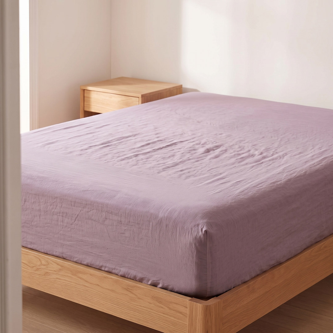 Linen Fitted Sheet – Deep Pocket in Mauve – seen from a doorway with wooden nightstand in corner