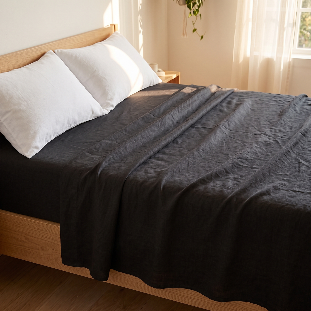 Linen Flat Sheet – Stone-Washed in Black – rumpled across bed with white pillows and hanging plant