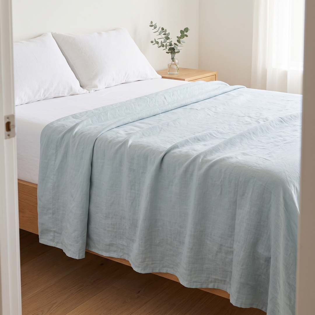 Linen Flat Sheet – Stone-Washed in Dusty Blue – seen through an open bedroom doorway, spread over white bedding