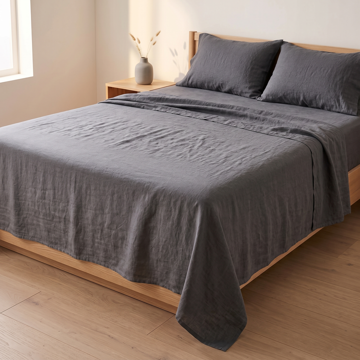Linen Flat Sheet Set – Stone-Washed, with 2 Pillowcases in Charcoal – angled view beside a nightstand with a vase of dried stems