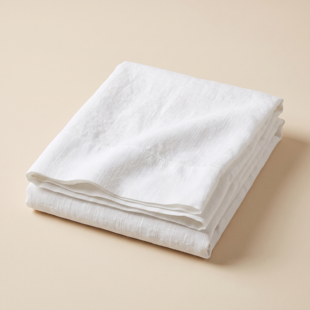 Linen Flat Sheet – Stone-Washed in White – neatly folded stack on a plain peach background