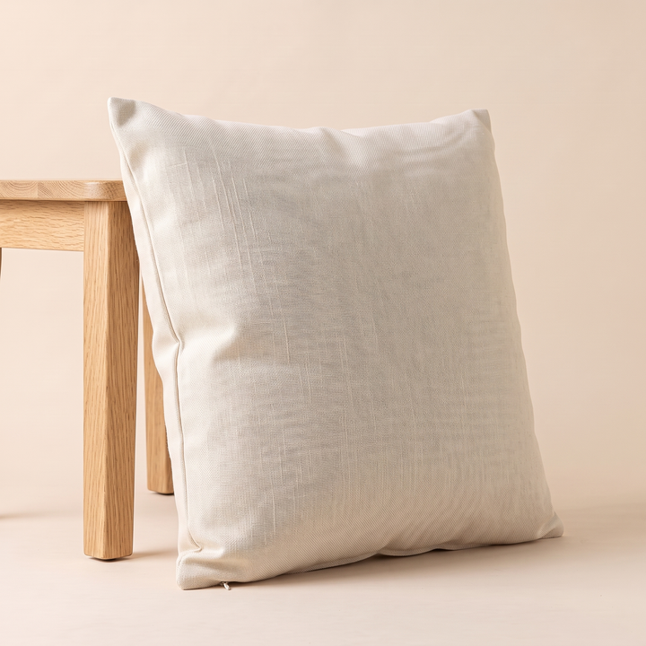 Linen-Look Pillow Cover in Cream – angled view leaning against a light wooden stool