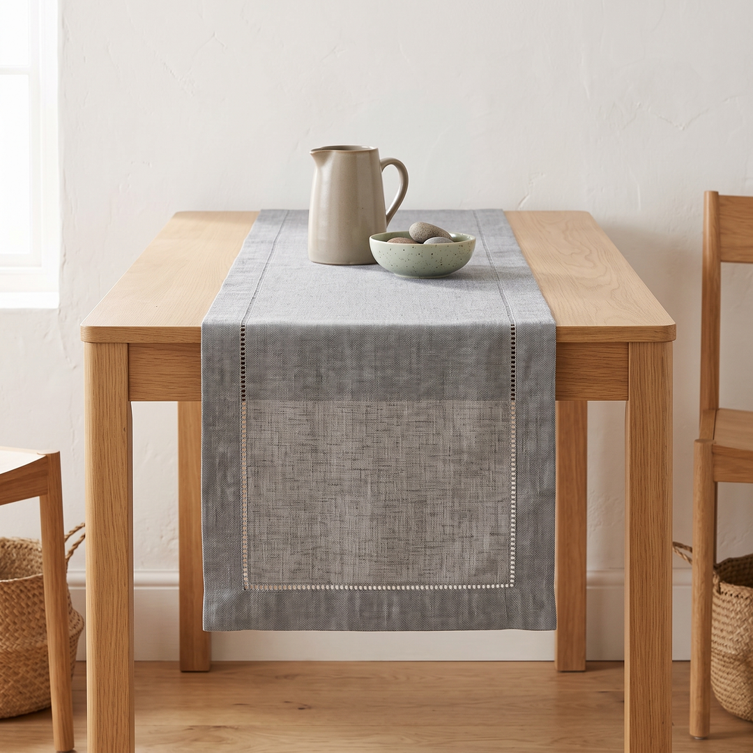 Linen-Look Table Runner – Hemstitch Border in Gray – straight-on with a pitcher and bowl of pebbles