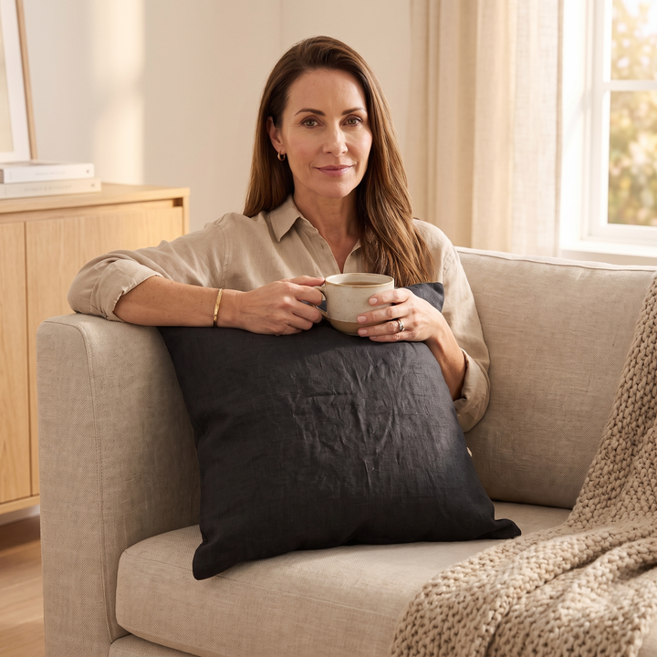 Linen Pillow Cover – 100% Linen in Black – held by a seated woman holding a mug on a sofa