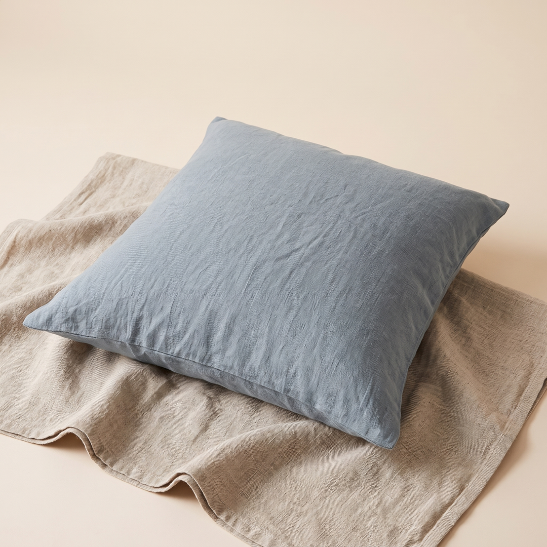 Linen Pillow Cover – 100% Linen in Dusty Blue – lying flat on a natural linen cloth, angled overhead view