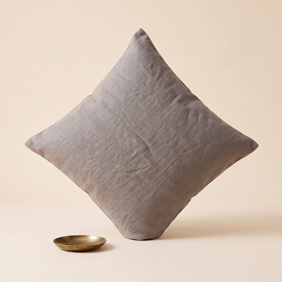 Linen Pillow Cover – 100% Linen in Gray – balanced on one corner beside a small brass dish