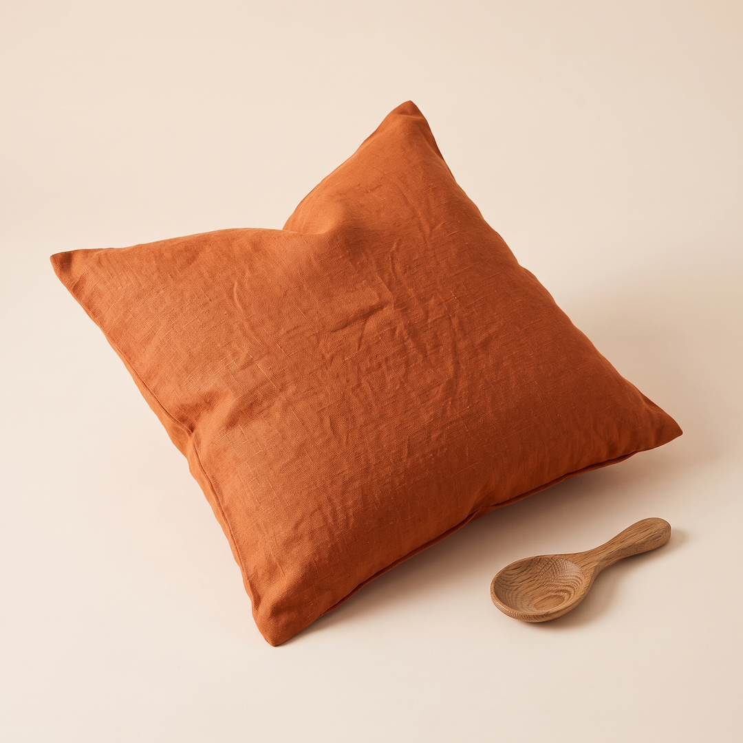 Linen Pillow Cover – 100% Linen in Rust – lying flat on cream surface beside a small wooden spoon