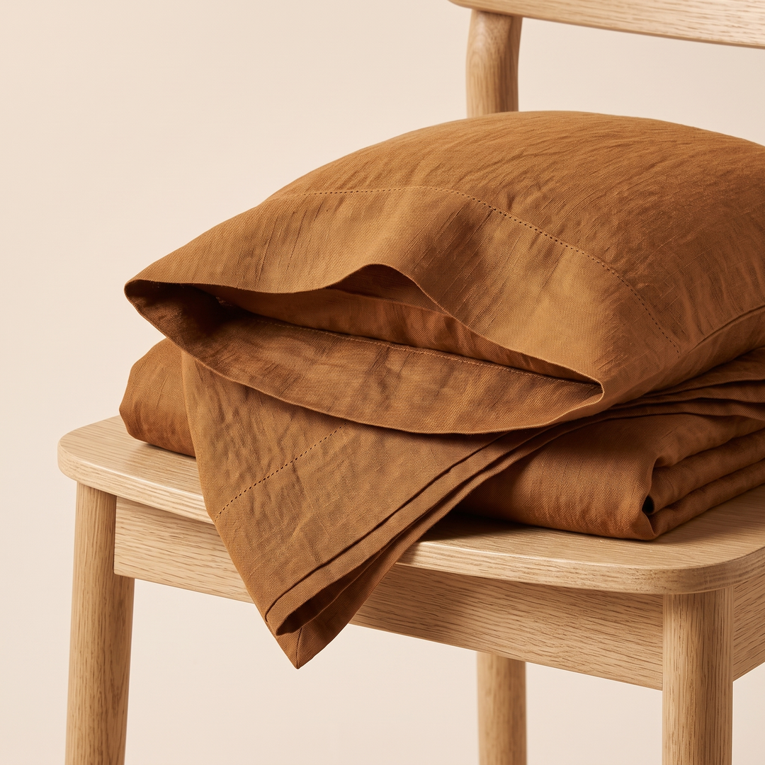 Linen Pillowcases – Set of 2 in Caramel – folded stack resting on a light wooden chair seat